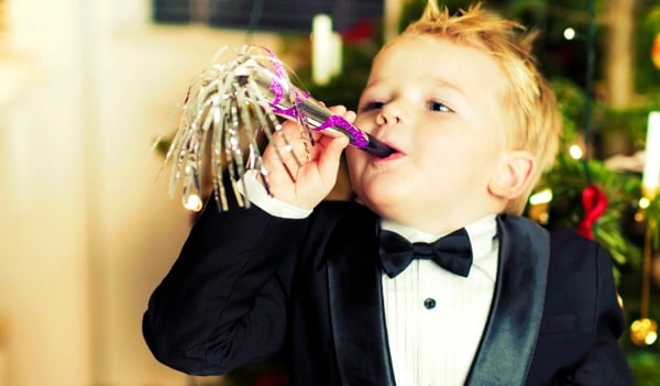 young boy dressed in a tuxedo blowing on a noisemaker for new years eve