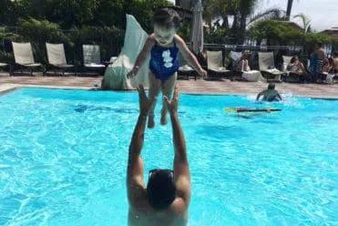 dad throwing little girl up in the air in pool