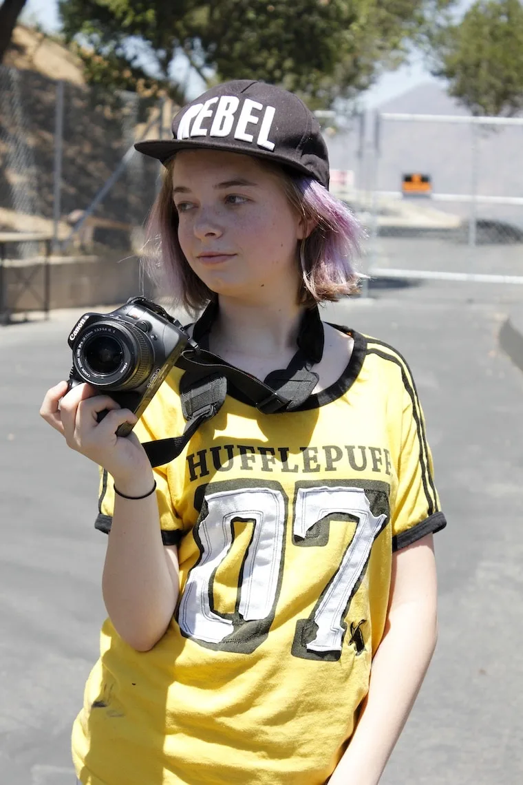 Amplify Sleep Away Camp girl wearing rebel hat and yellow shirt holding camera