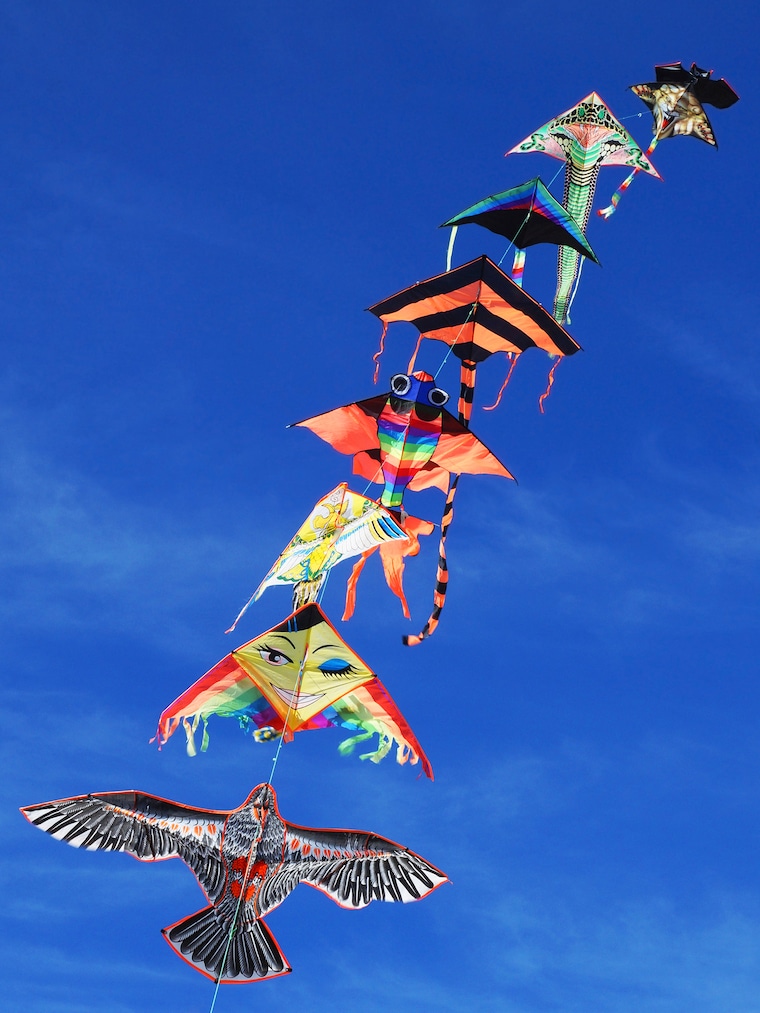 long string of kites flying in blue sky