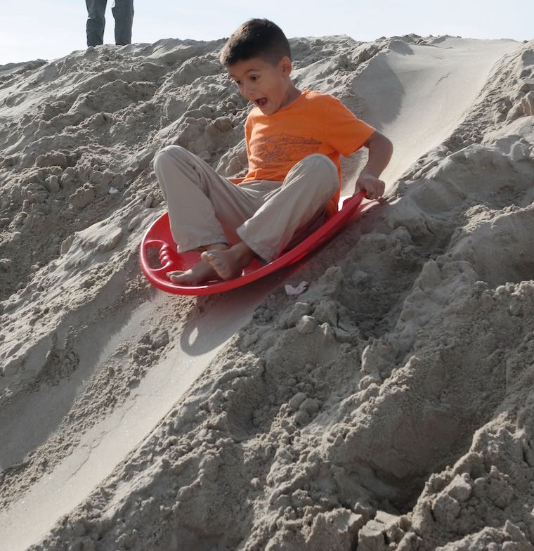 kid coming down a sand berm on a sled