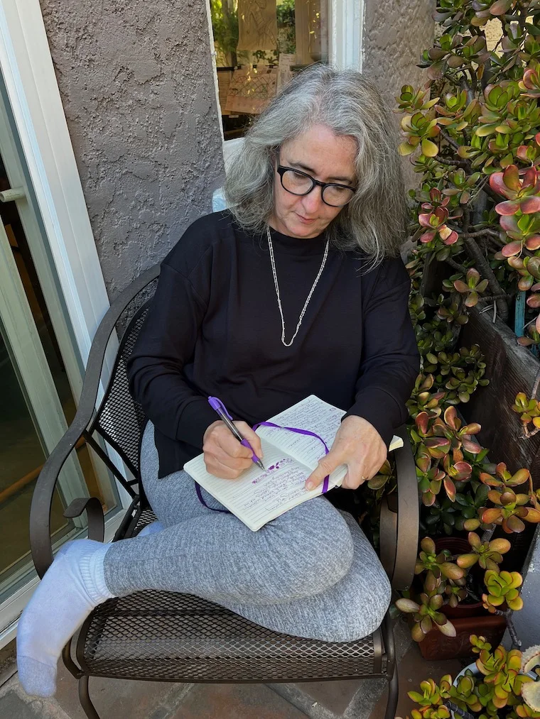 a woman sitting outdoors, writing in a journal