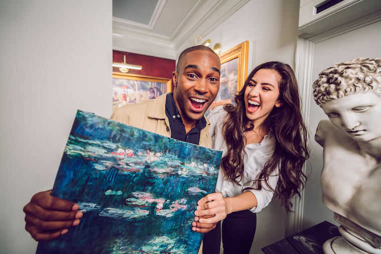 two people laughing and holding a painting as part of an escape game