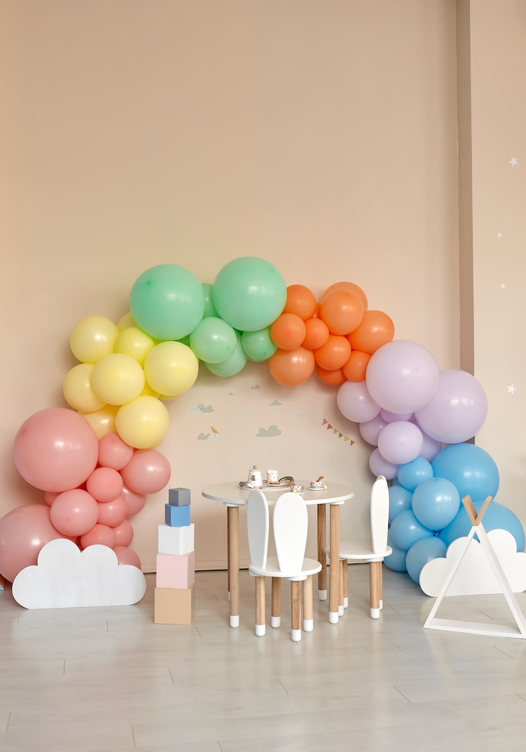Small table and chairs with bunny ears in children's room interior. Rainbow, colorful balloon arch, decoration in honor of the holiday, birthday, party