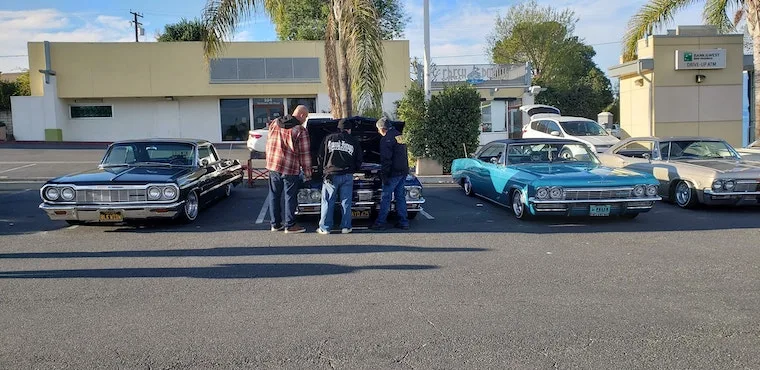 men looking under the hood of a car at a local car show