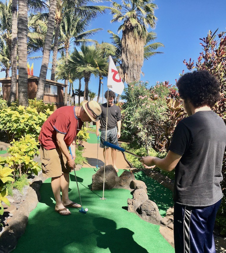 father and 2 sons playing mini golf
