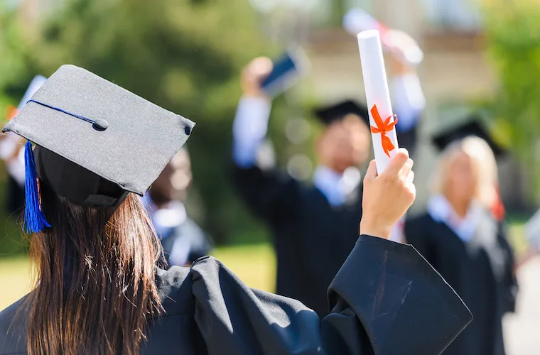 high school graduation girl wearing graduation cap holding a paper diploma 