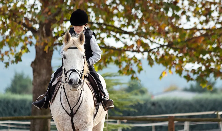 Kid riding white horse during horseback lessons.