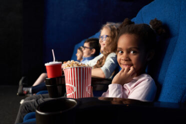 Cute girl sitting in cinema with friends, looking at camera.