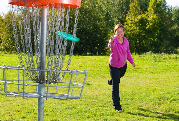 woman throwing disc into disc basket in disc golf