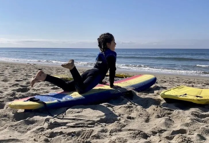 kid lying on a surfboard in the sand featured image activities