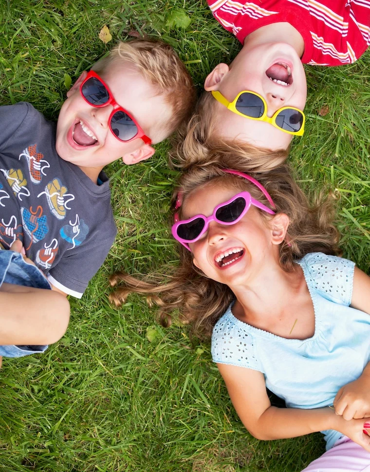 3 toddlers lying in the grass laughing