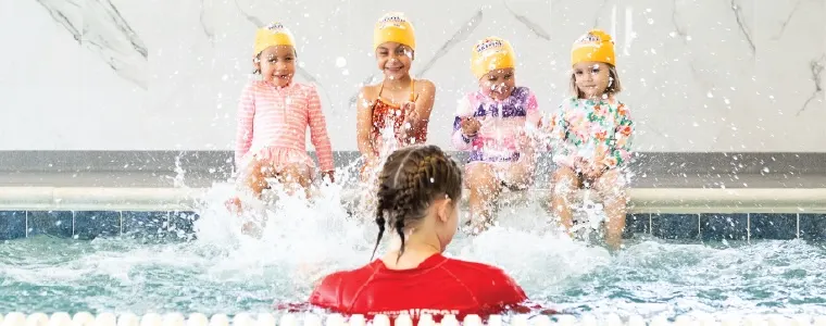 girls splashing on the side of the pool with instructor photo courtesy of British Swim School of Westside Los Angeles - Hawthorne