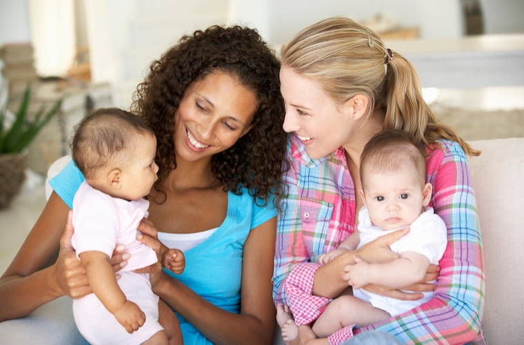 Two Young Mothers holding babies and smailing